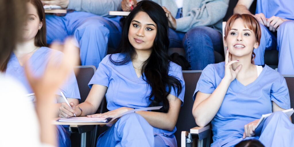 A group of women in scrubs sitting in an auditorium away from home.