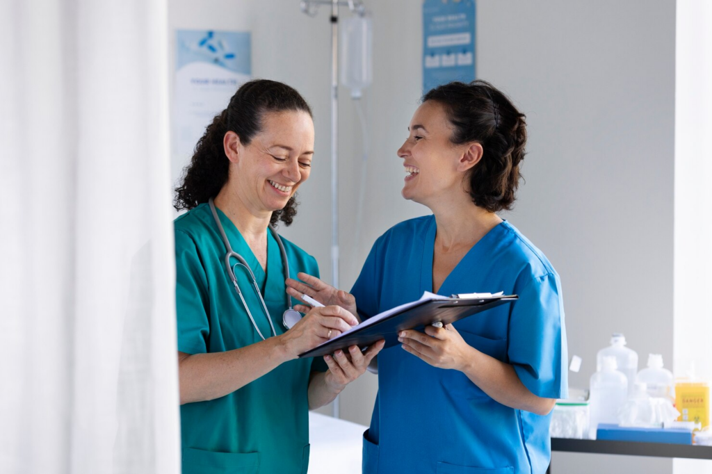 Two healthcare professionals in scrubs smiling and discussing a patient's chart in an urgent care clinic setting.