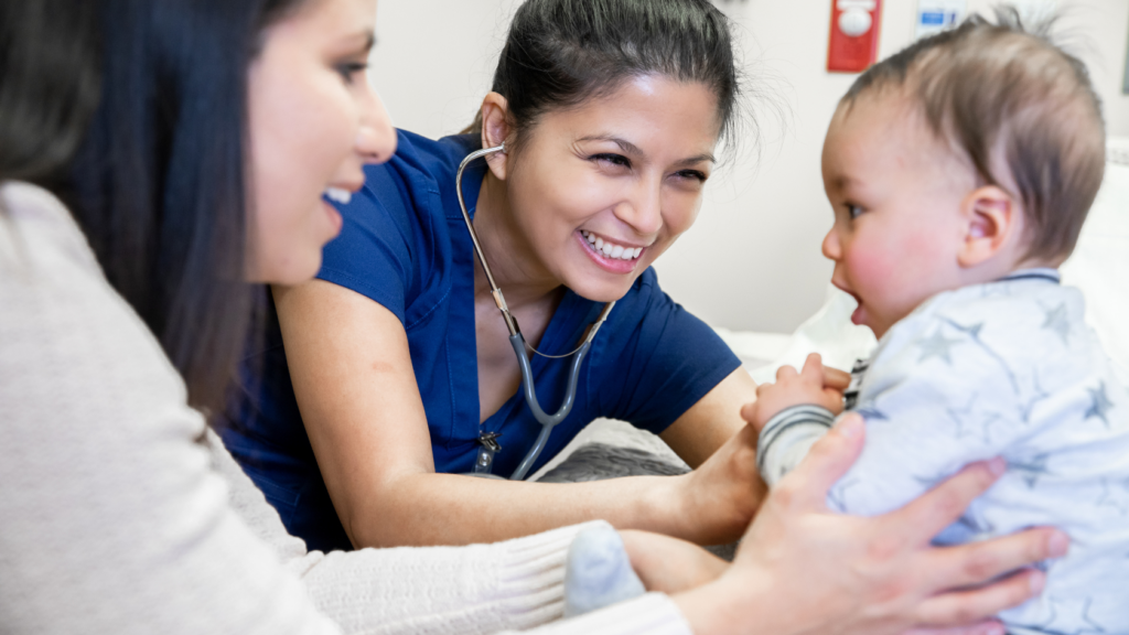 A nurse practitioner with a stethoscope and a woman interact with a baby in a clinical setting, highlighting the importance of primary care in pediatrics.