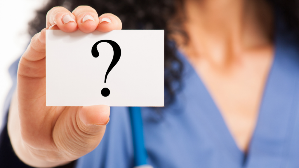 A nurse practitioner in a blue top holds up a white card with a large question mark on it, embodying the essence of impostor syndrome.