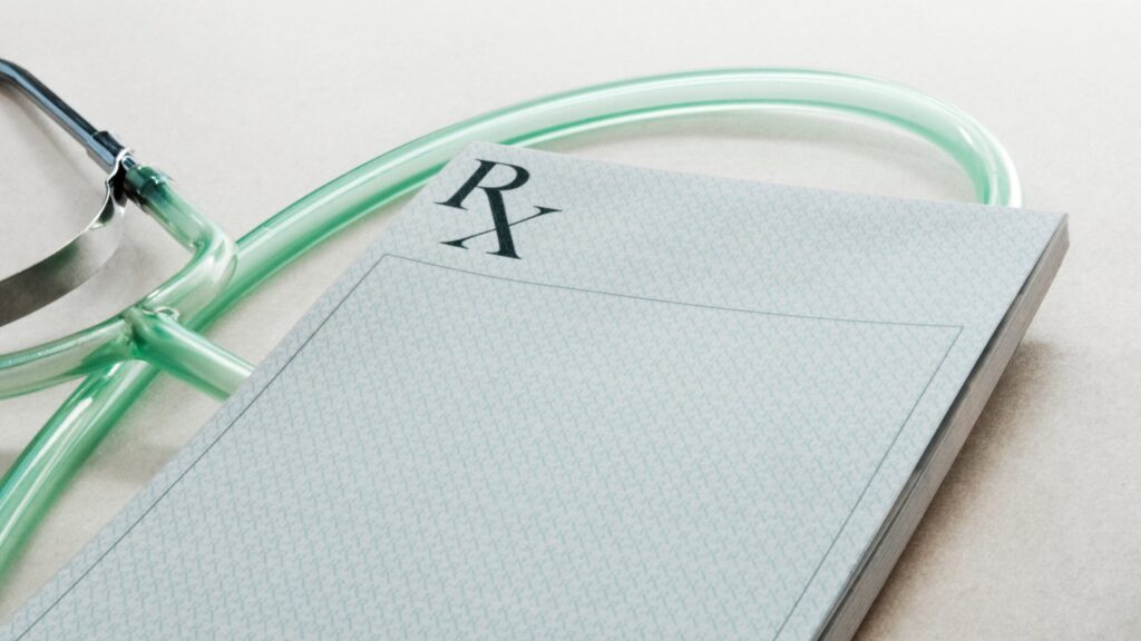 A blank prescription pad marked "RX" lies next to a green stethoscope on a light surface, symbolizing clinical autonomy and the importance of being a better teammate in healthcare.