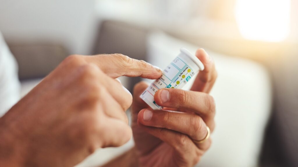 A person holds a prescription pill bottle and points to the label, appearing to read the medication instructions carefully—highlighting the importance of avoiding medical errors.